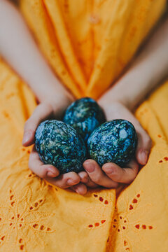 Hands holding blue Easter eggs dyed with hibiscus on yellow dress
