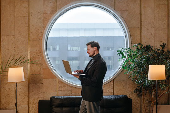 Businessman standing in loft office using laptop by round window