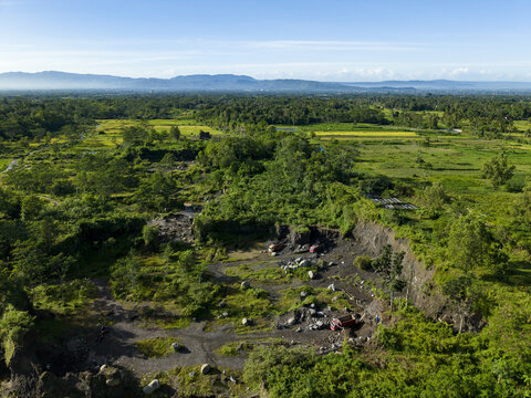 Aerial view of a rugged quarry with dark, rocky terrain contrasting against the vibrant green vegetation, Klaten Regency, Central Java, Indonesia.