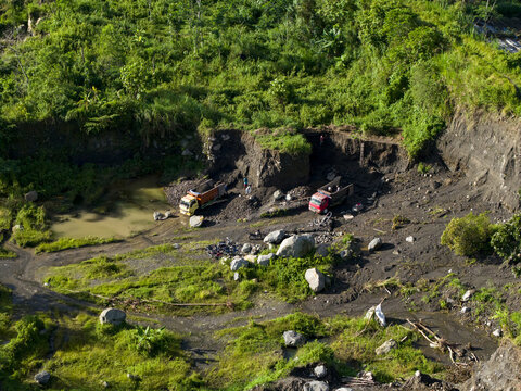 Aerial view of the Woro River area showing earthmoving equipment amid a landscape scarred by quarrying and lush vegetation, Klaten Regency, Central Java, Indonesia.