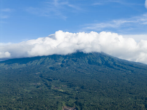 Aerial view of Mount Merapi's verdant slopes meeting the sky, partially veiled by fluffy white clouds, a breathtaking contrast of green and blue, Klaten Regency, Central Java, Indonesia.
