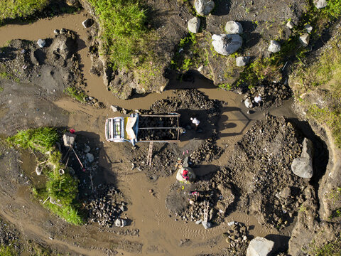 Aerial view of a truck navigating the muddy terrain near Woro River, contrasting the dark earth with the bright vehicle, Klaten Regency, Central Java, Indonesia.