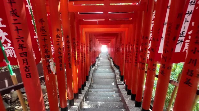 Walking down staircase through rows of red torii gates at Hie Shrine in Tokyo, Japan with sunlight and green trees