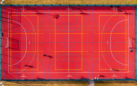 Aerial view of the vibrant red multi-court shimmers, sharply contrasted by the bright white and yellow lines, shadows dancing across the surface, Warsaw, Masovian Voivodeship, Poland.