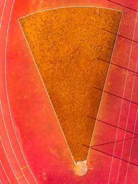 Aerial view of a vibrant sports field, where concentric red tracks encircle a striking mustard-colored sector, creating a dynamic contrast, Warsaw, Masovian Voivodeship, Poland.