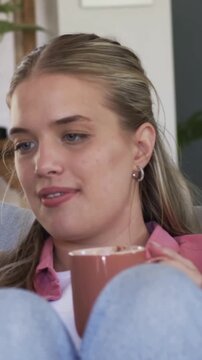 Vertical video: Camera framing shifting, woman holding ceramic mug smiling and laughing on sofa