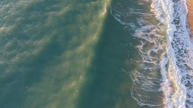 Aerial drone landscape showing sea waves and sandy beach forming beautiful coastal patterns.
