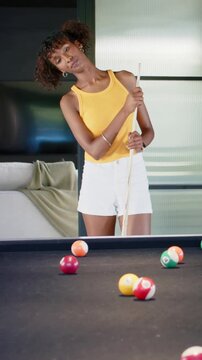 Vertical video: Shifting woman in yellow tank checking angles striking cue ball on black felt table