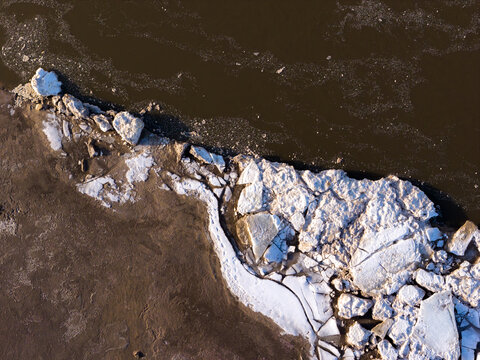 Aerial view of the frozen Vistula River, with stark white ice floes contrasting against the dark water and the muddy shore, Warsaw, Masovian Voivodeship, Poland.