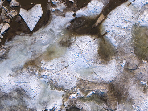 Aerial view of the frigid Vistula River's icy embrace, its frozen surface cracked and fractured into a mosaic of stark white and shadowy depths, Warsaw, Masovian Voivodeship, Poland.