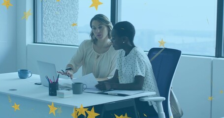 Pointing two coworkers in blouses working over laptop and documents at bright office with coffee