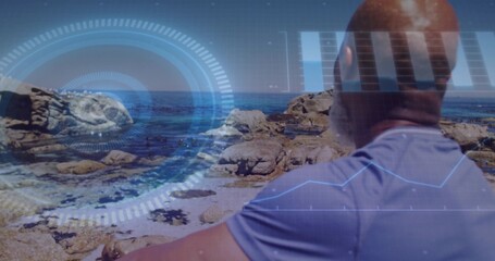 Standing mature man wearing purple shirt watching rocky coastline and HUD graphics, copy space