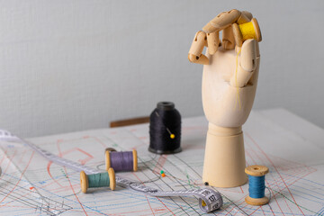 Wooden hand holding yellow thread spool upright on pattern, concept of new sewing project and creative idea © Mariia