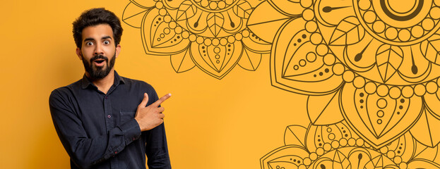 A man stands in a bright room and points to a large mandala design on the wall. He looks surprised and excited. The wall is painted in a vibrant yellow color. © Prostock-studio