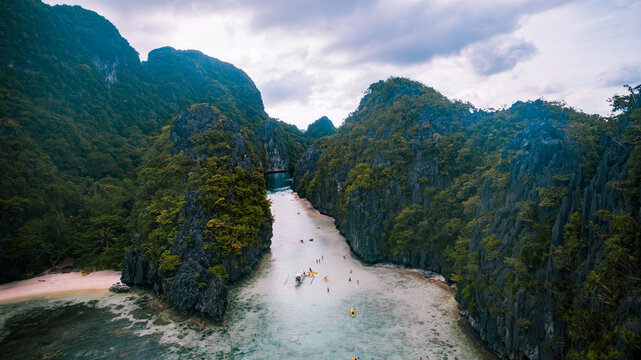 Aerial view of dramatic limestone cliffs cloaked in verdant foliage embrace the turquoise waters, creating a stunning contrast of textures and tones, El Nido, Mimaropa, Philippines.