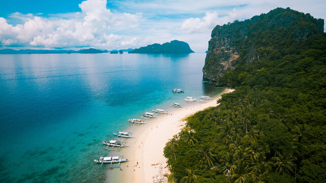 Aerial view of boats lined up on the shore, where turquoise waters meet the lush green foliage, creating a tropical haven, El Nido, Mimaropa, Philippines.