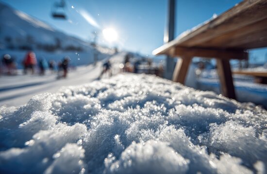 Sunlit snow sparkles on a ski slope with a wooden bench in foreground