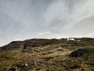 Rocky hillside under cloudy sky in Scotland with rugged terrain and sparse vegetation