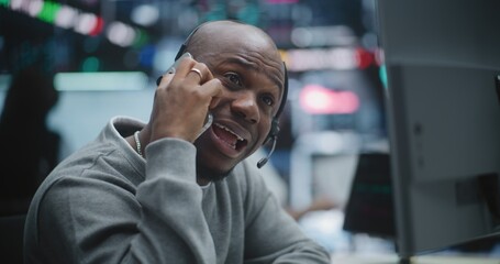 Obraz premium Black Male Broker Engages in Heated Smartphone Conversation, Gesturing Wildly Falling Charts on Multi Monitors. Man Pure Despair, Panic Witnesses Massive Market Collapse, Profit Loss in Trading Hub.