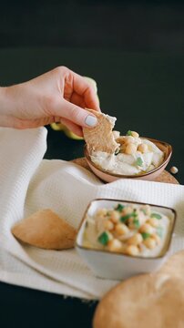 Close up of female hand dipping fresh pita bread into homemade creamy hummus.