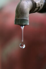 Water drop dripping from an old tap, a symbol of freshness and conservation. The water is clear, and the faucet is aged and rustic, against a soft blurred background