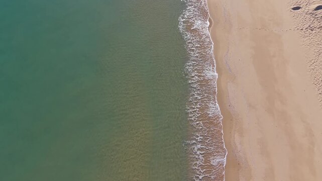 Drone aerial shot of calm green sea meeting sandy beach forming natural coastline pattern with gentle ocean waves.