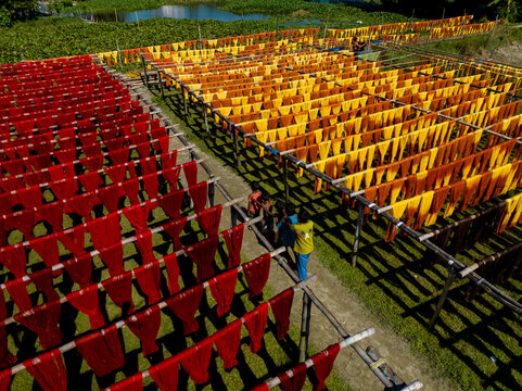Aerial view of vibrant red and golden fabrics drying in geometric patterns under the sun, creating a striking contrast of colors and textures, Narayanganj, Dhaka Division, Bangladesh.