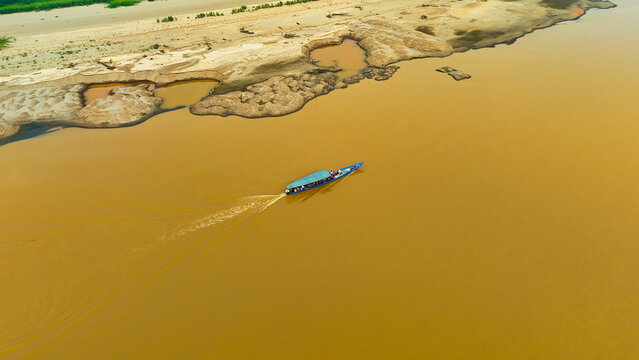 Aerial view of a boat sailing on the murky river contrasting with the textures of the eroded riverbank, Puerto Maldonado, Madre de Dios, Peru.
