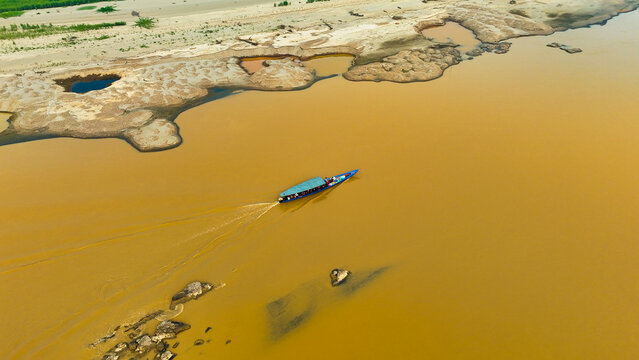Aerial view of a boat sailing on the muddy river contrasting with the light brown sandy shore, Puerto Maldonado, Madre de Dios, Peru.