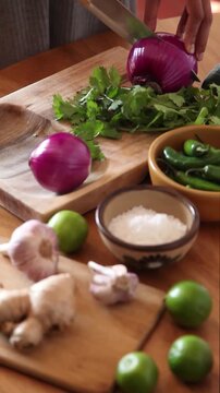 Close up of a person's hands slicing a fresh onion on a wooden cutting board.