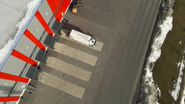 Aerial view of a logistics truck preparing to reverse into a warehouse loading dock at a modern distribution center during daytime operations.