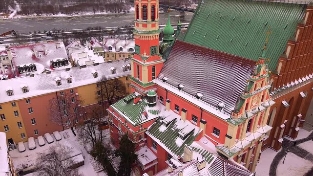 Aerial footage moving past the colorful jesuit church, revealing the snowy rooftops of warsaw's old town and the vistula river