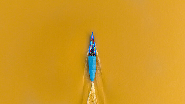 Aerial view of a vibrant blue boat slicing through the muddy river waters, leaving a foamy wake behind, Puerto Maldonado, Madre de Dios, Peru.