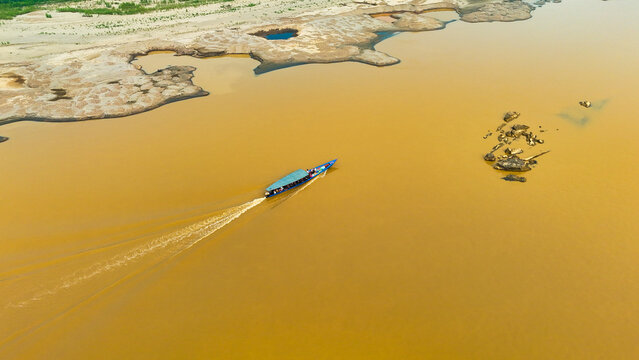 Aerial view of a boat slicing through the muddy river, leaving a white wake against the ochre water near the sandy shores, Puerto Maldonado, Madre de Dios, Peru.