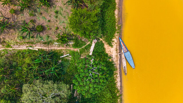 Aerial view of two boats resting on the sandy bank where the ochre river meets the lush jungle, Puerto Maldonado, Madre de Dios, Peru.