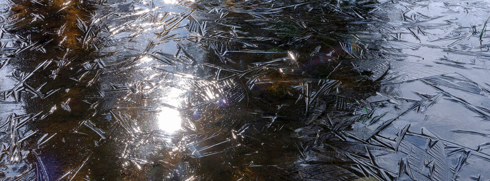 Sunlight reflects off a thin layer of ice forming intricate patterns on a body of water. Adamello Brenta Natural Park, Madonna di Campiglio,Trentino,Italy