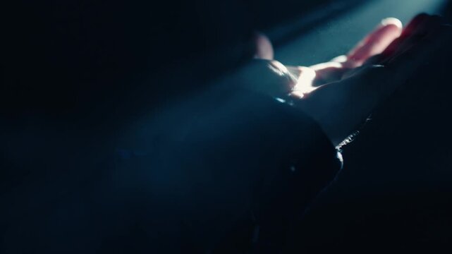 A hand reaches out to touch a concentrated beam of light in a pitch-black setting. The illumination highlights the contours of the fingers as they interact with the glowing ray.