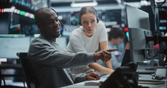 Two Professional Brokers Analyzing Big Data Trends on Multi Monitor Dashboard. Man Gestures Towards Specific Chart on Monitors While Woman Provides Input. Strategic Planning in Modern Fintech Office.