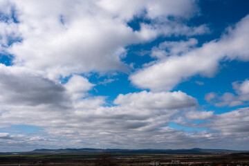 Wide panoramic view of a bright blue sky filled with fluffy white cumulus clouds over a distant mountain horizon.