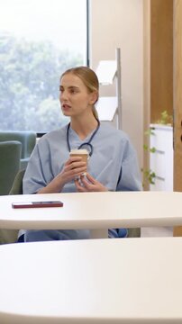 Vertical video: Holding coffee, nurse in scrubs talking on break at staffroom as peer placing cup