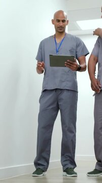 Vertical video: Seeing third pass, two in grey scrubs checking tablet in corridor near yellow bin