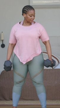 Vertical video: Starting woman in workout top doing hinge row to tone in bedroom with hex dumbbells