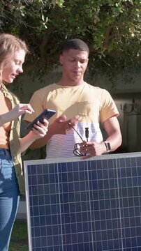 Vertical video: Tapping phone, pair in casual clothes checking panel connector in yard aiming sun