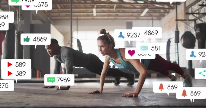 Doing synced push-ups in gym with hanging bags, man dark top, woman teal tank, notifications rising