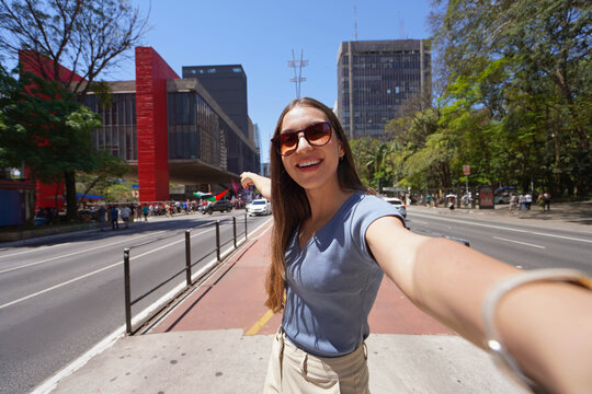 Young woman with sunglasses taking a selfie pointing MASP Museum on Paulista Avenue in Sao Paulo, Brazil