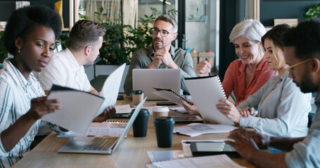 Fototapeta premium Man, team and discussion for documents at startup for review, planning or laptop at media company. People, editor and group with talk for proposal, feedback or project management at creative agency