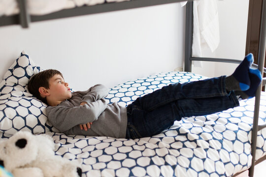Side view of a young Boy lying on top of a bed with his arms folded daydreaming