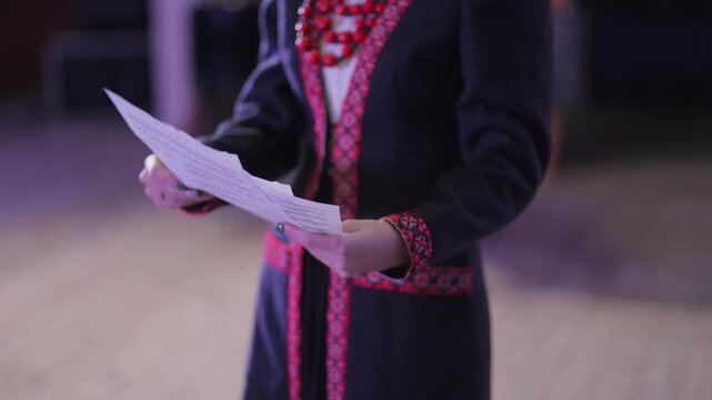 Woman reading notes on stage wearing embroidered coat
