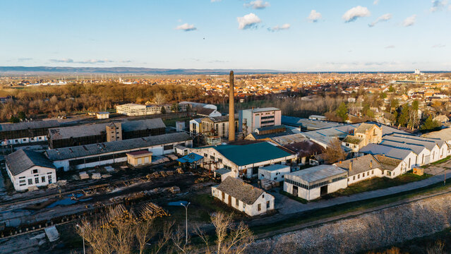 Aerial view of a factory complex, its chimney reaching for the sky amidst a sprawling urban landscape, juxtaposing industrial might with the serene horizon, Sremska Mitrovica, Vojvodina, Serbia.