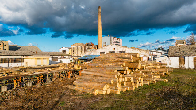 Aerial view of logs stacked high under a moody sky, contrasting sharply with the industrial buildings and tall chimney, Sremska Mitrovica, Vojvodina, Serbia.